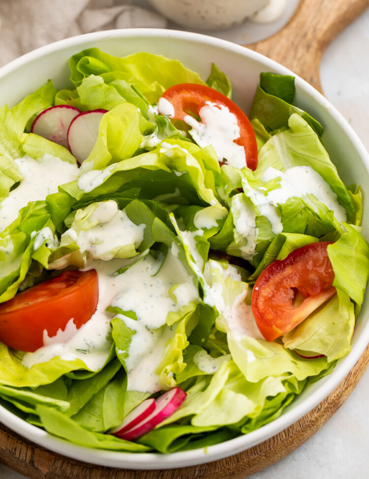 Overhead, angled view of a house salad with buttermilk ranch dressing and large slices of tomatoes.