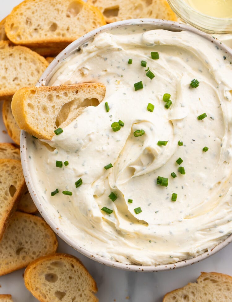 A piece of crisp crostini laying in a bowl of creamy homemade boursin cheese.