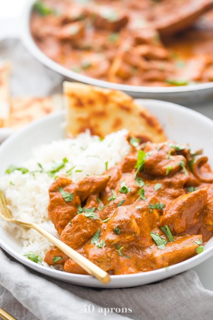 Best chicken tikka masala recipe over rice with naan in a white bowl with skillet in the background