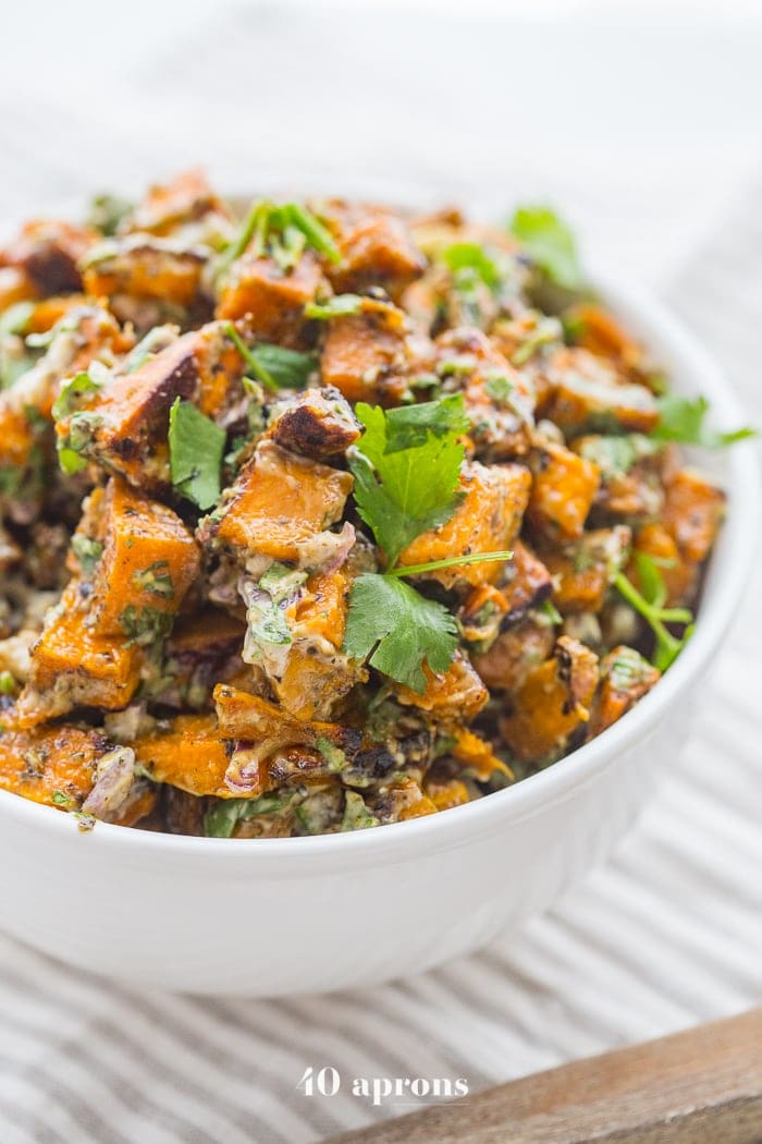This herb roasted Whole30 sweet potato salad is perfection: crispy sweet potatoes coated in a rich and creamy herb mixture, topped with crunchy red onions. Perfect at a Whole30 picnic, alongside a Whole30 dinner recipe, or as a lunch side dish all week long, you'll love how flavorful this roasted Whole30 sweet potato salad is. Elegant enough for company but easy enough for a weeknight! Vegan option to make this an herb roasted vegan sweet potato salad, too.
