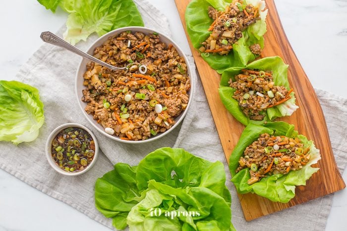 Healthy PF Changs lettuce wraps recipe on a board with a bowl of filling to the side and lettuce leaves