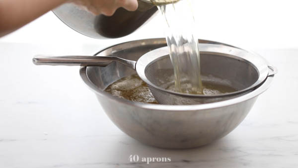 Strained bone broth through a mesh strainer over a silver bowl