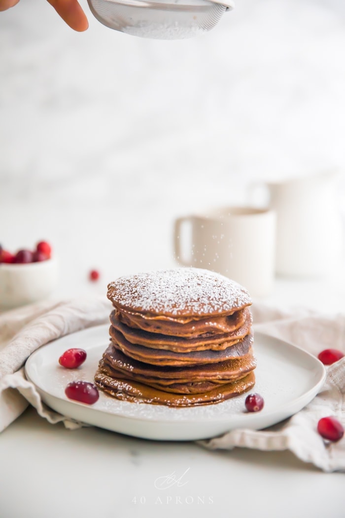 Stack of paleo gingerbread pancakes on a white plate with powdered sugar on top and fresh cranberries as garnish