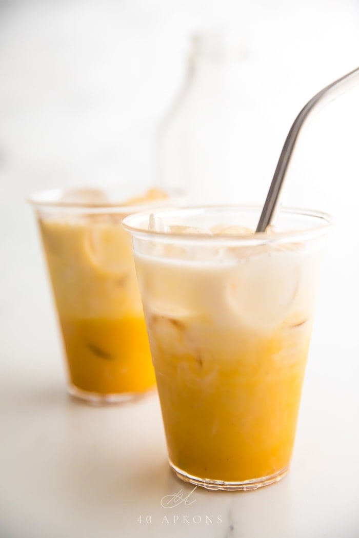 Two iced golden milks in clear plastic cups with straws