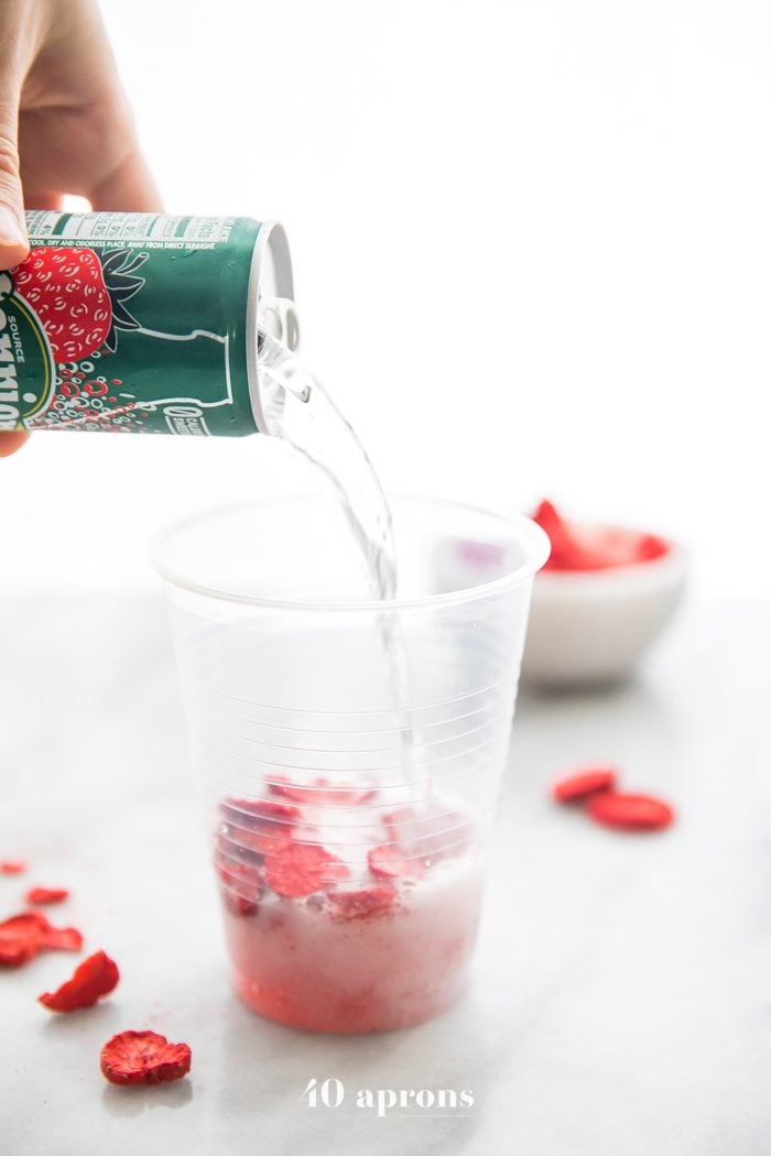 Perrier strawberry sparkling water pouring over freeze-dried strawberries for healthy pink drink