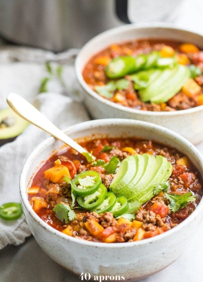 Two bowls of Instant Pot Whole30 chili with butternut squash topped with jalapenos and avocados with Instant Pot in background
