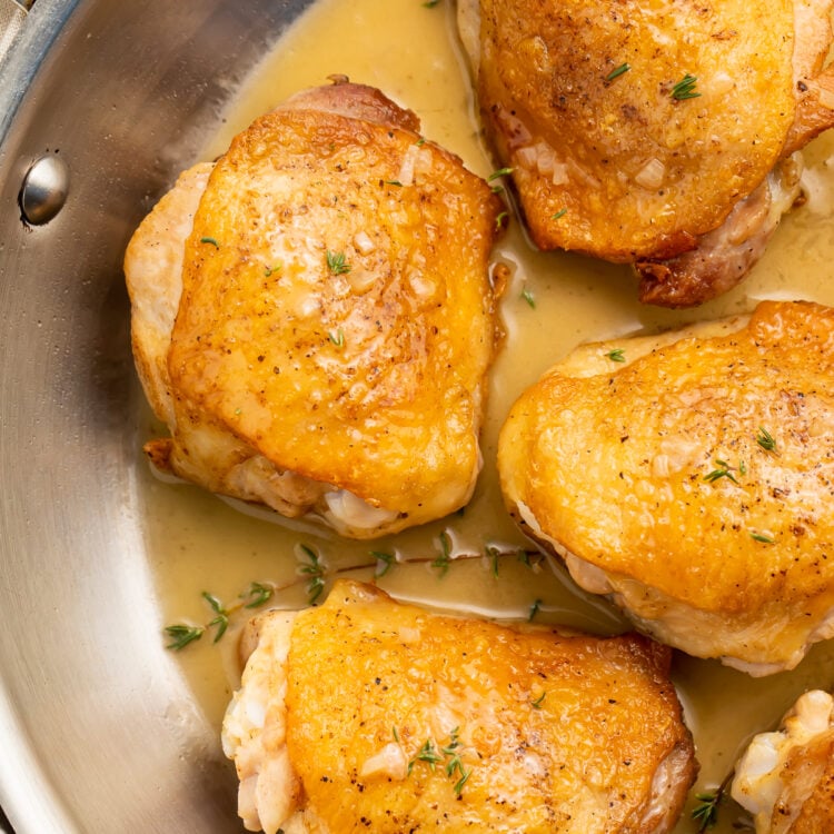 Pan-seared chicken thighs in a simple pan sauce, resting in a silver saucepan.