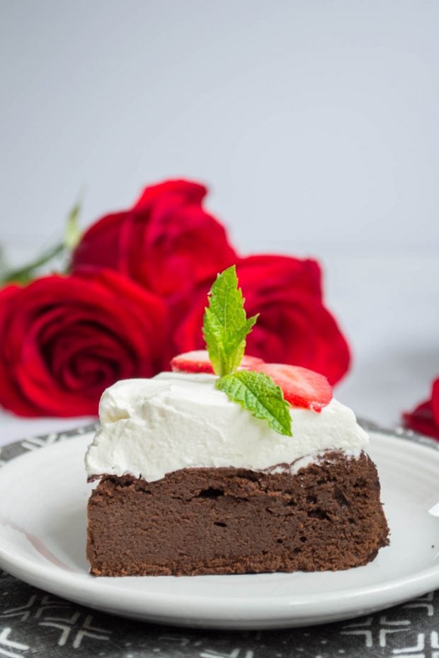 side view of a slice of keto flourless chocolate cake with whipped cream on a white plate