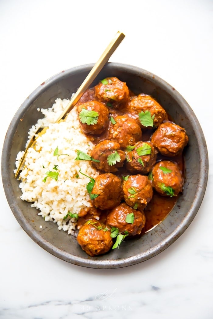 Indian meatballs with creamy sauce next to cauliflower rice topped with cilantro in a grey dish