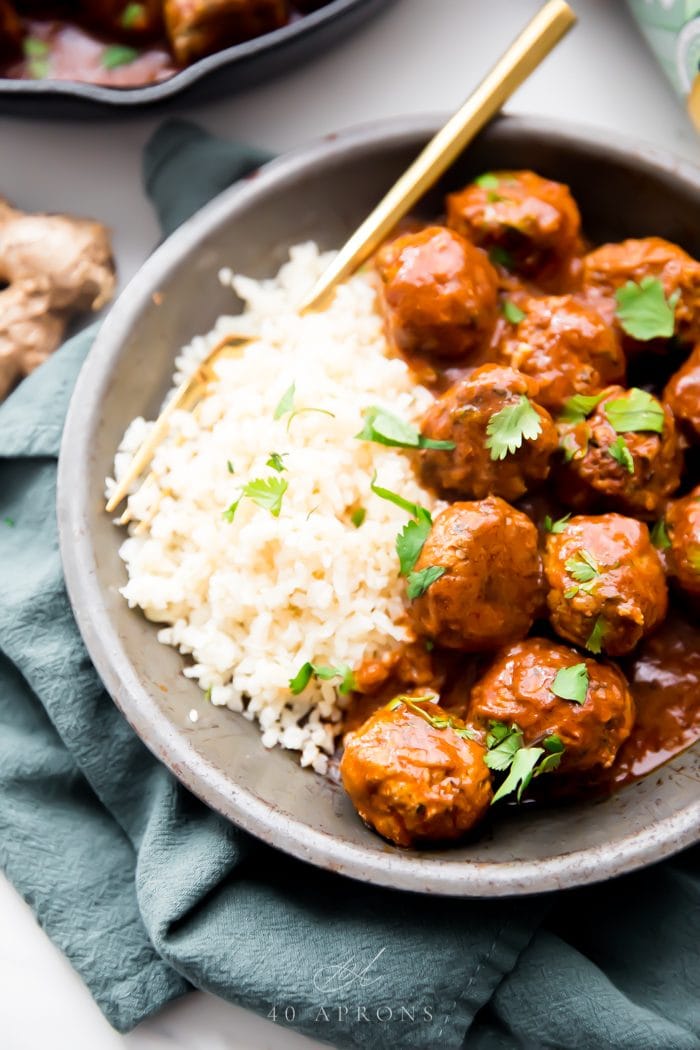 Indian meatballs with creamy sauce next to cauliflower rice topped with cilantro in a grey dish on a green napkin
