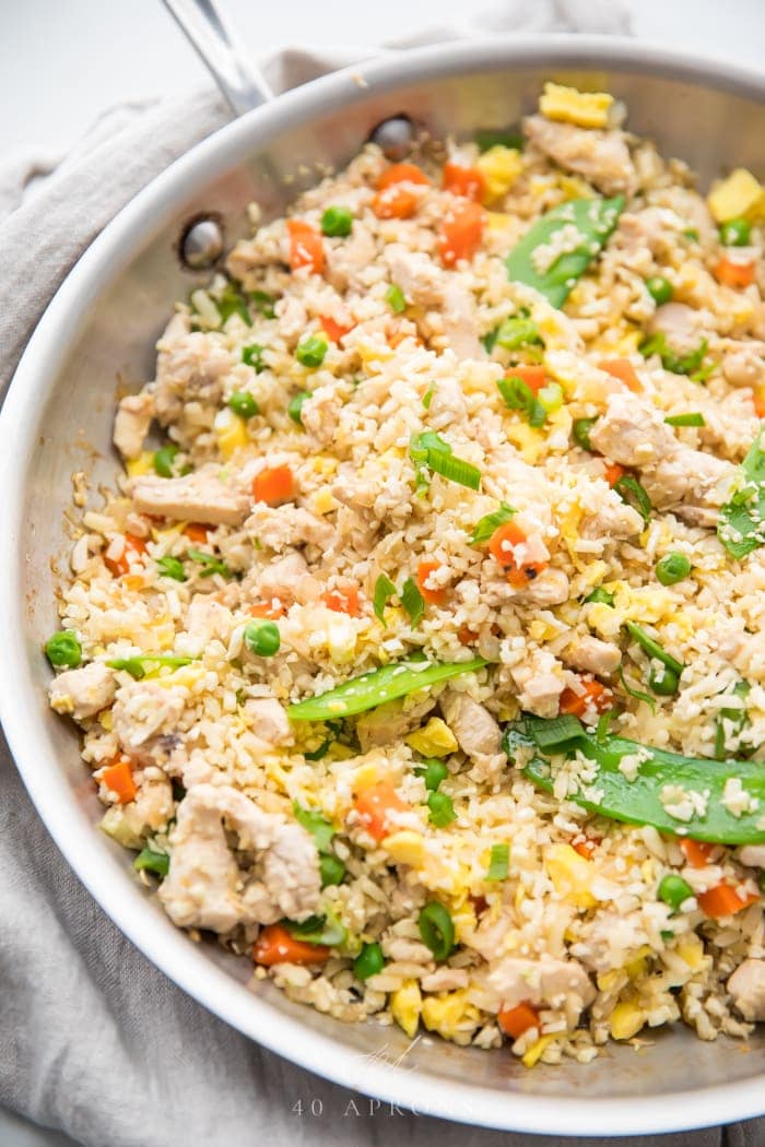 A skillet of cauliflower fried rice with chicken, peas, carrots, snow peas