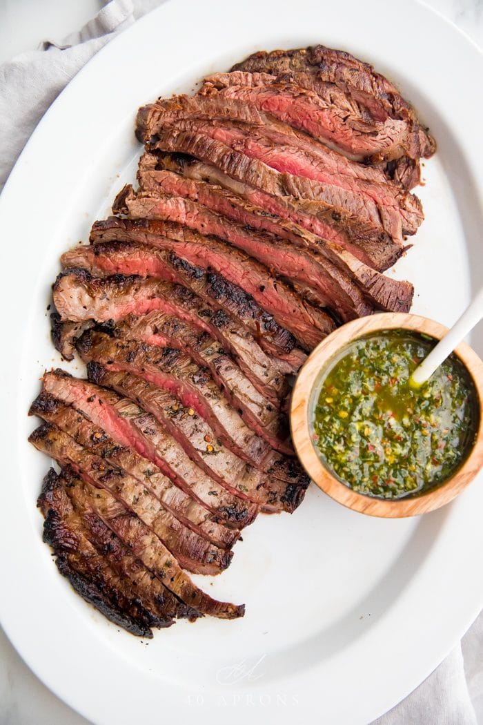 A flank steak cut into strips against the grain with a bowl of chimichurri sauce to the side