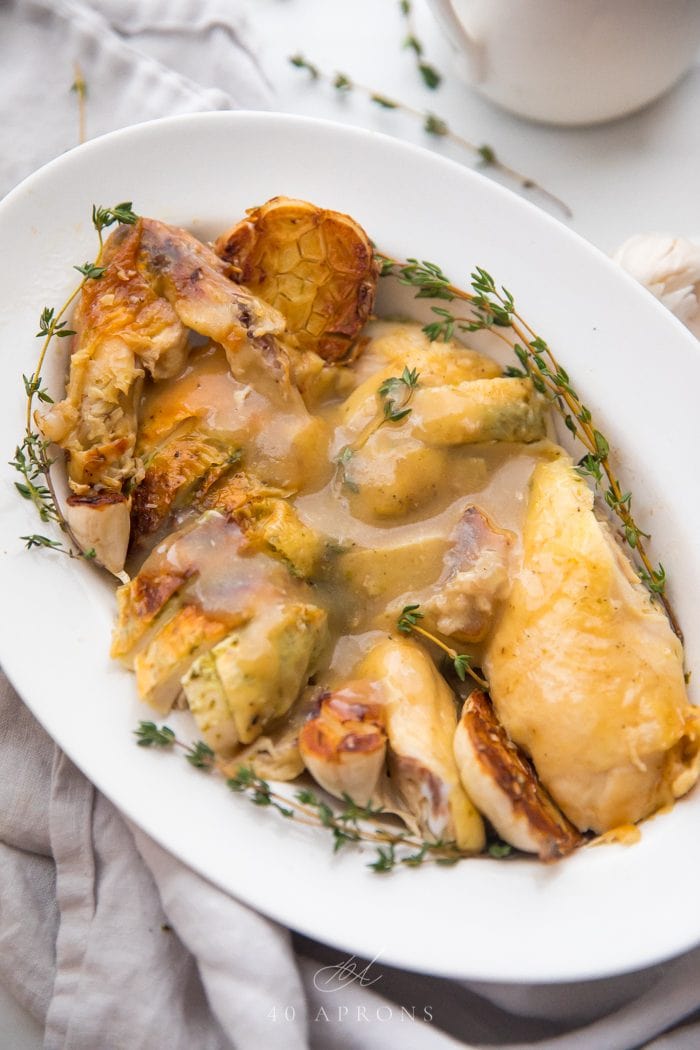 Slow cooker roast chicken cut into pieces topped with gravy and garnished with fresh thyme