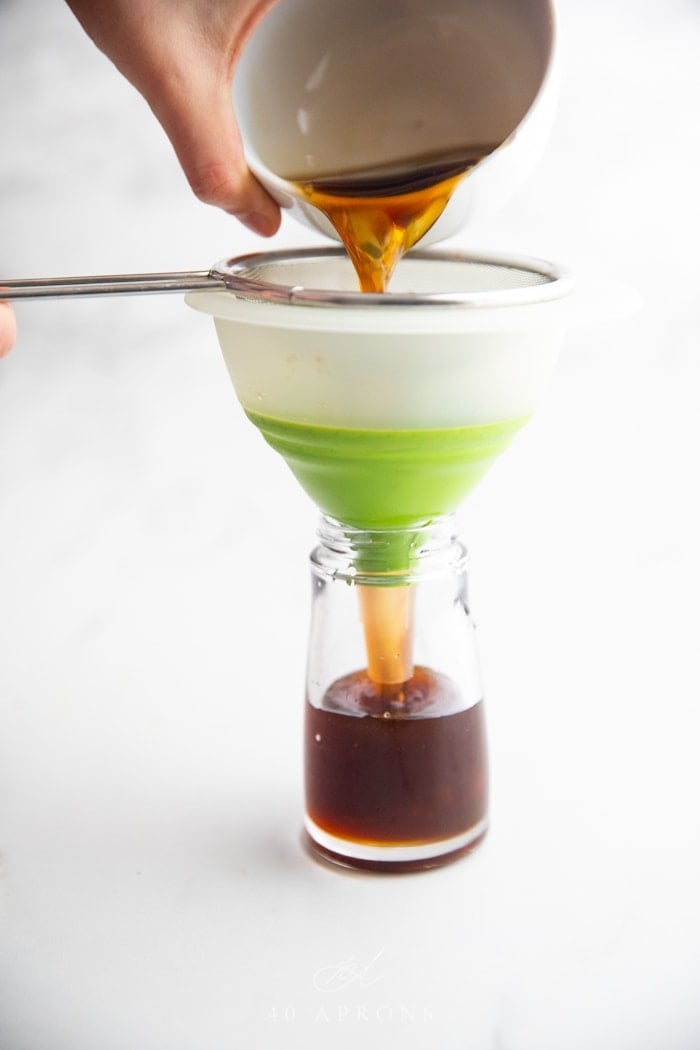A bowl of soy sauce substitute pouring over a sieve, through a funnel, into a bottle