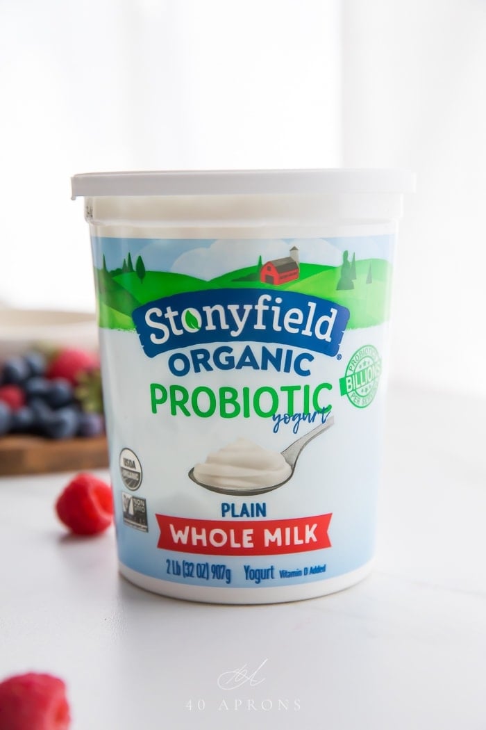 A container of Stonyfield Organic Plain Whole Milk Yogurt with berries in background