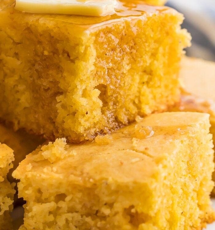 Gluten free cornbread stacked on a white plate with butter and honey