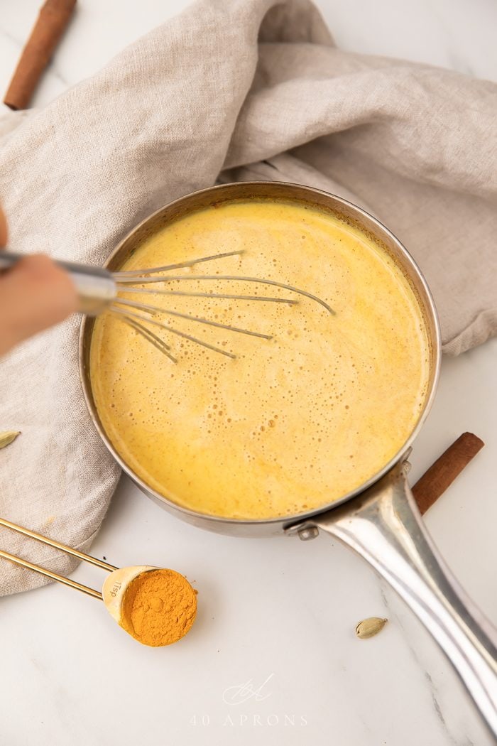 Whisk stirring golden milk in a saucepan