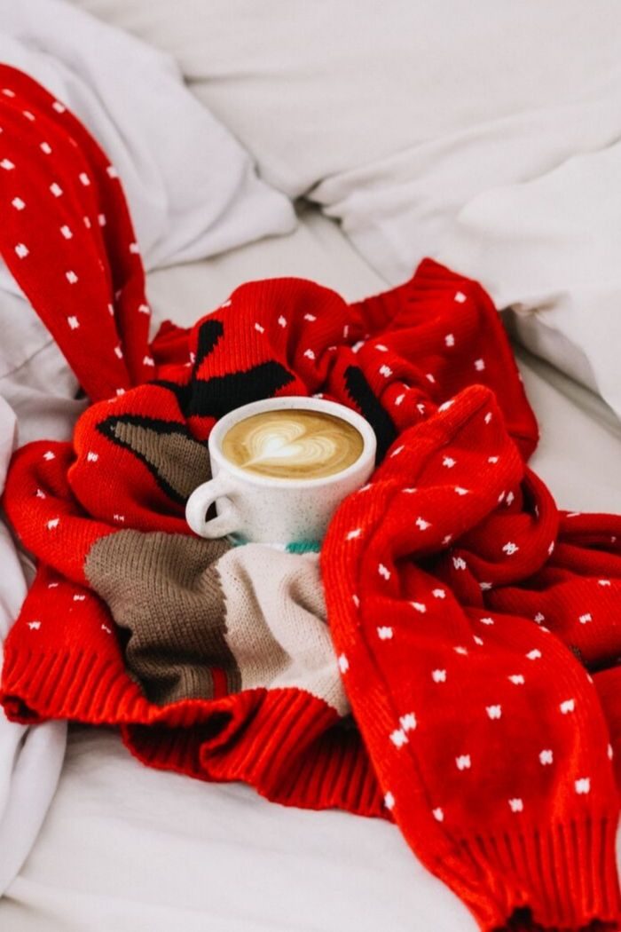 a mug of cappuccino nestled into a red Christmas Sweater on a bed