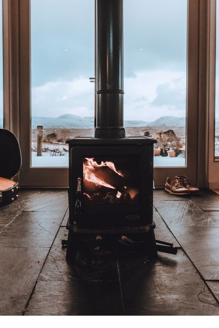 a black Swedish fireplace in front of a big window overlooking a snow-filled landscape