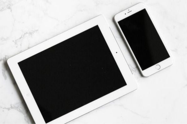 a  turned off white tablet and a white smartphone on a marble countertop