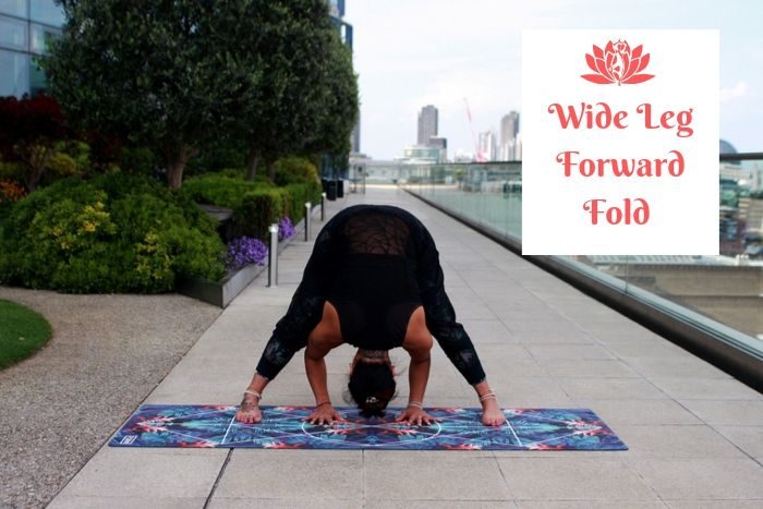 a man holding the yoga detox position of the wide leg forward fold with a city panorama in the background 