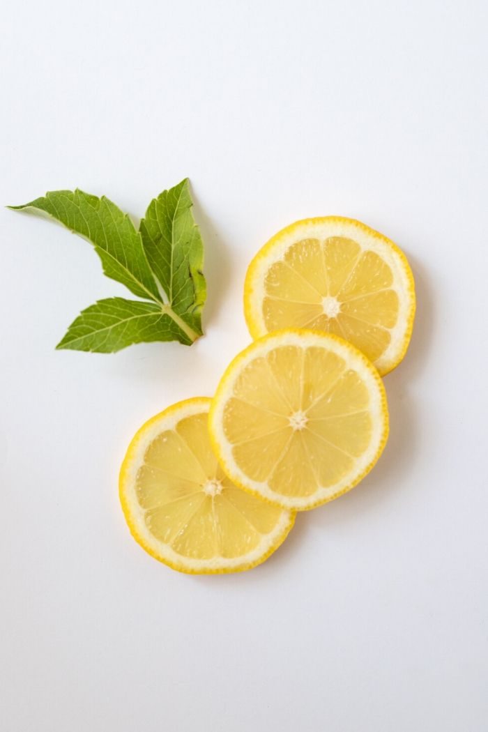 three slices of lemon and some mint leaves against a white background