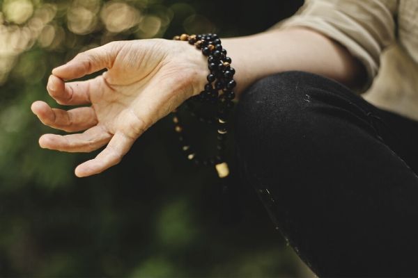 a hand in the gyan meditation hand gesture with prayer beads wrapped around the wrist 