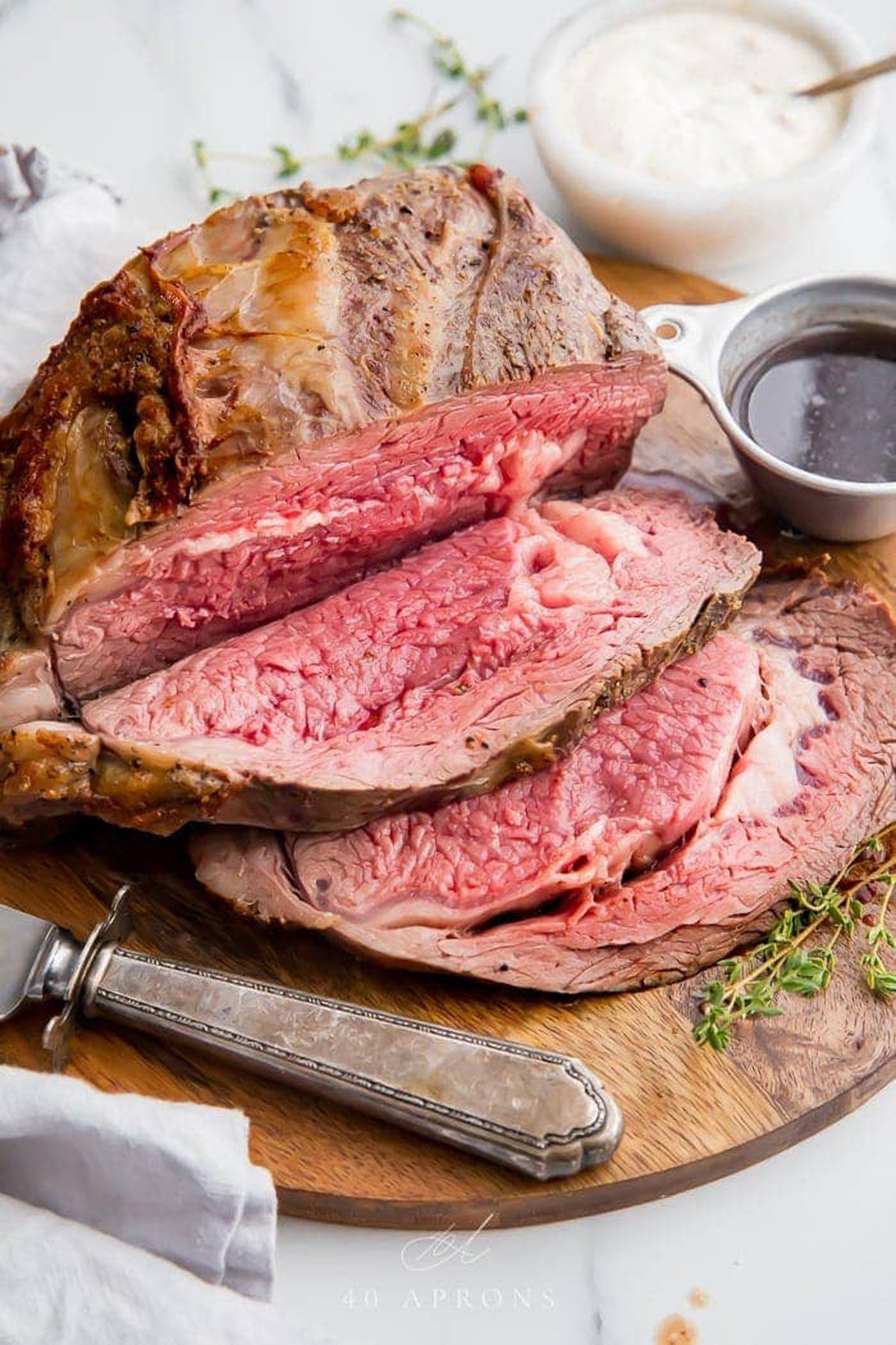 Carved, juicy prime rib resting on a wooden cutting board next to a small silver ramekin of au jus.