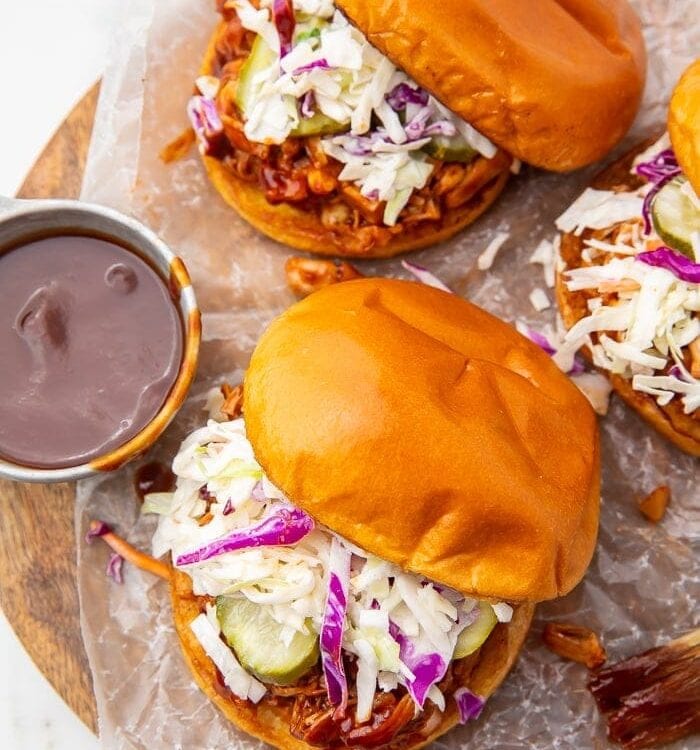 Three vegan BBQ jackfruit sandwiches with a side of barbecue sauce