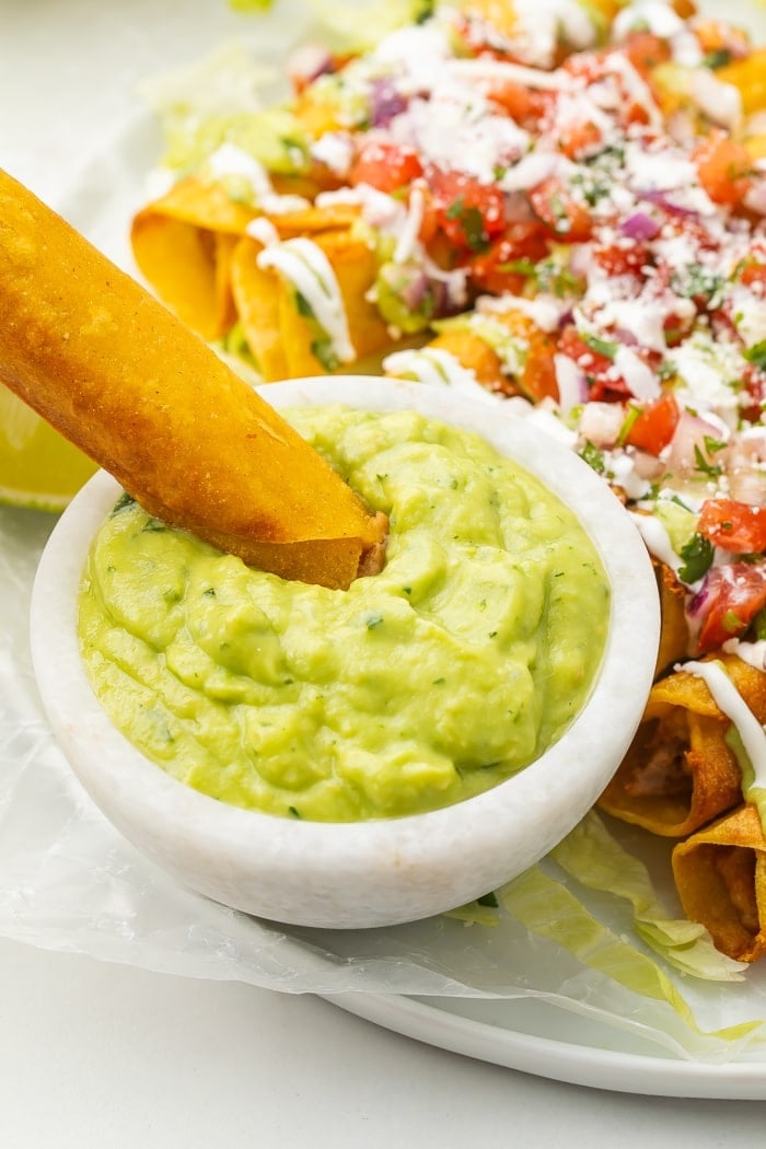 Bean and cheese taquito being dipped in avocado salsa