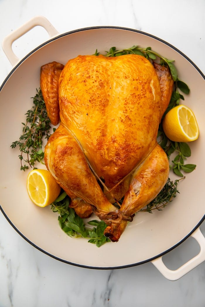Chicken brine on a whole chicken on a plate with lemons and herbs