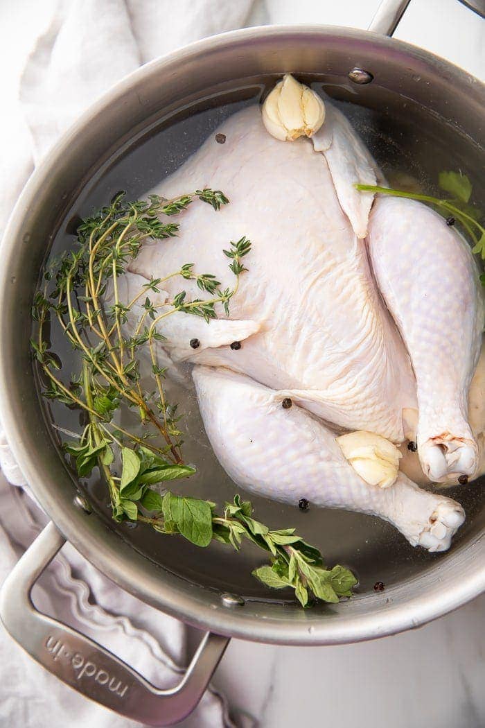Chicken brine being made with a full chicken in a pot with herbs and water