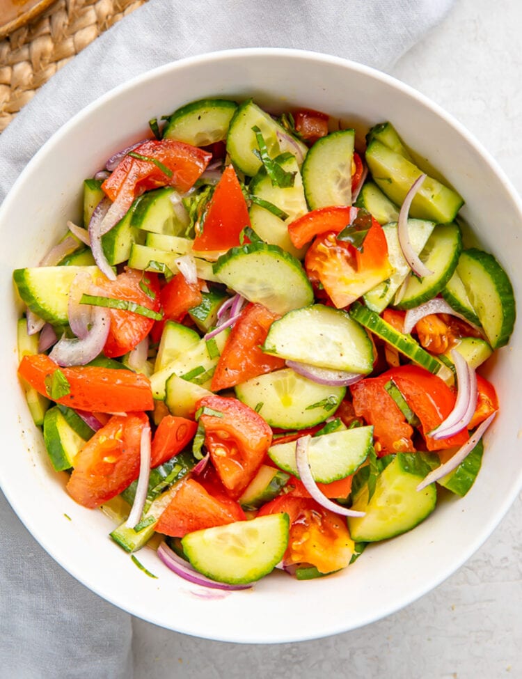 Top-down view of a large white bowl holding a fresh, vibrant cucumber tomato salad with slices of red onion.