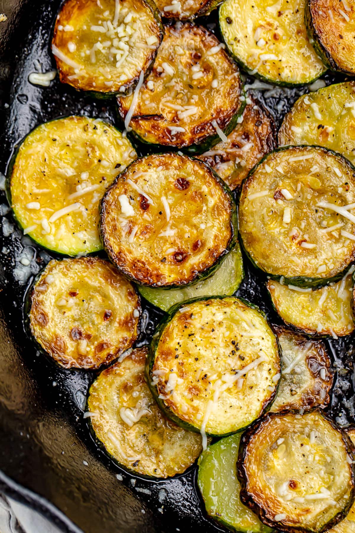Close-up of crispy sauteed zucchini discs topped with finely shredded cheese.