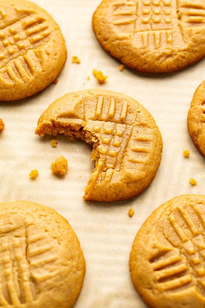 Keto peanut butter cookies on parchment paper with a bite taken out of one