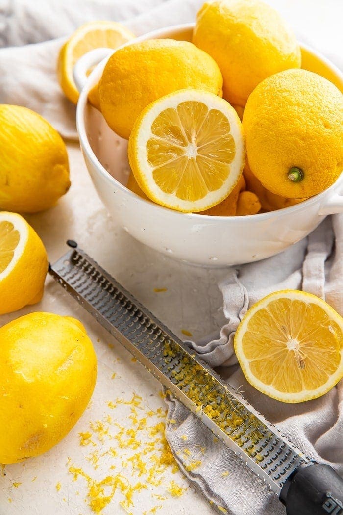a bowl of lemons surrounded by sliced lemons, a microplane, and lemon zest
