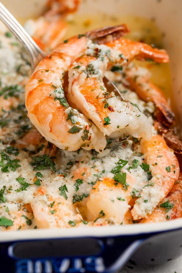 Baked shrimp being spooned out of a baking dish