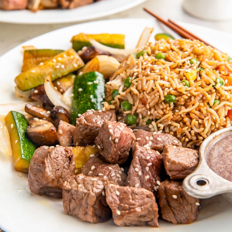 A plate of hibachi steak in sauce with stir-fry vegetables and a mound of delicious fried rice.