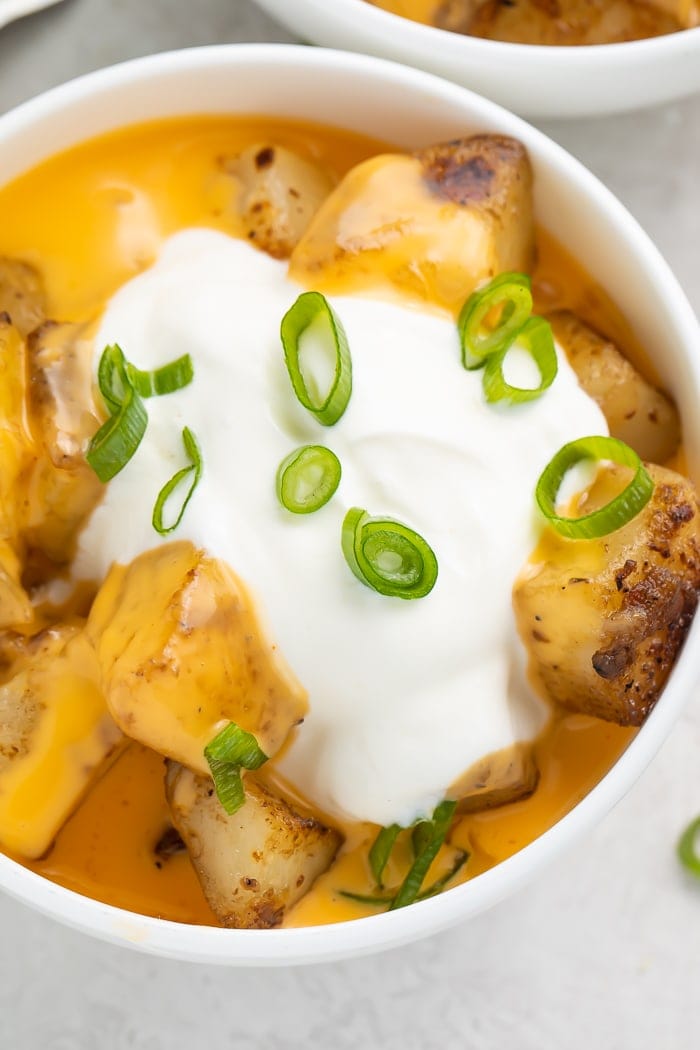 Close-up of cheesy fiesta potatoes in a bowl with a dollop of sour cream and sliced green onions