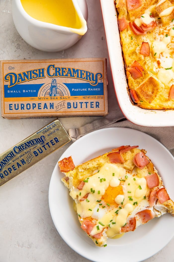 A slice of eggs benedict casserole on a white plate surrounded by a stick of Danish Creamery butter and a kraft box of butter