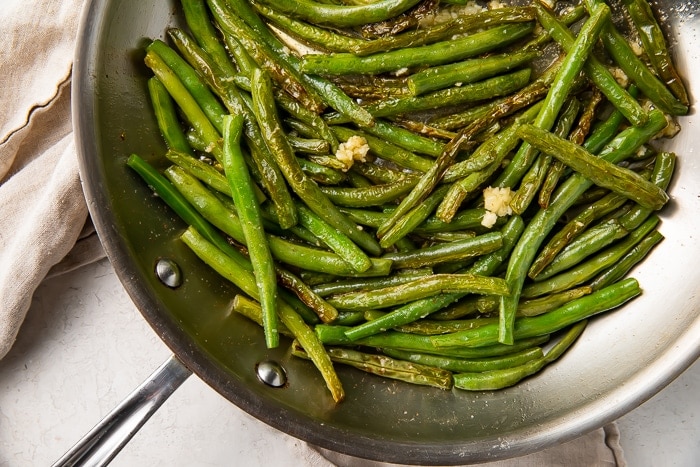 overhead shot of a skillet with cooked green beans, lemon zest, and garlic