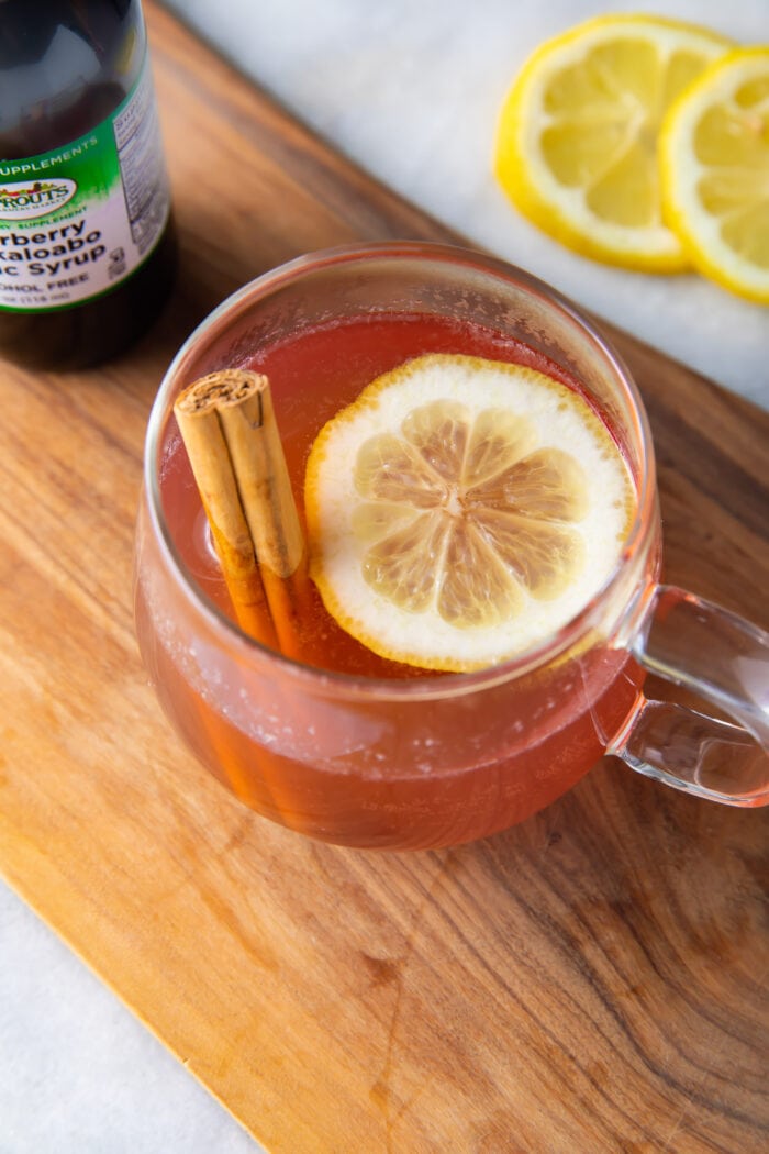 Elderberry hot toddy on a wooden plank next to lemon slices and a bottle of elderberry syrup