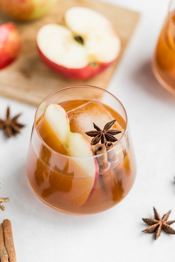 Apple cider cocktail in a stemless wine glass with cinnamon sticks, star anise, and sliced apples