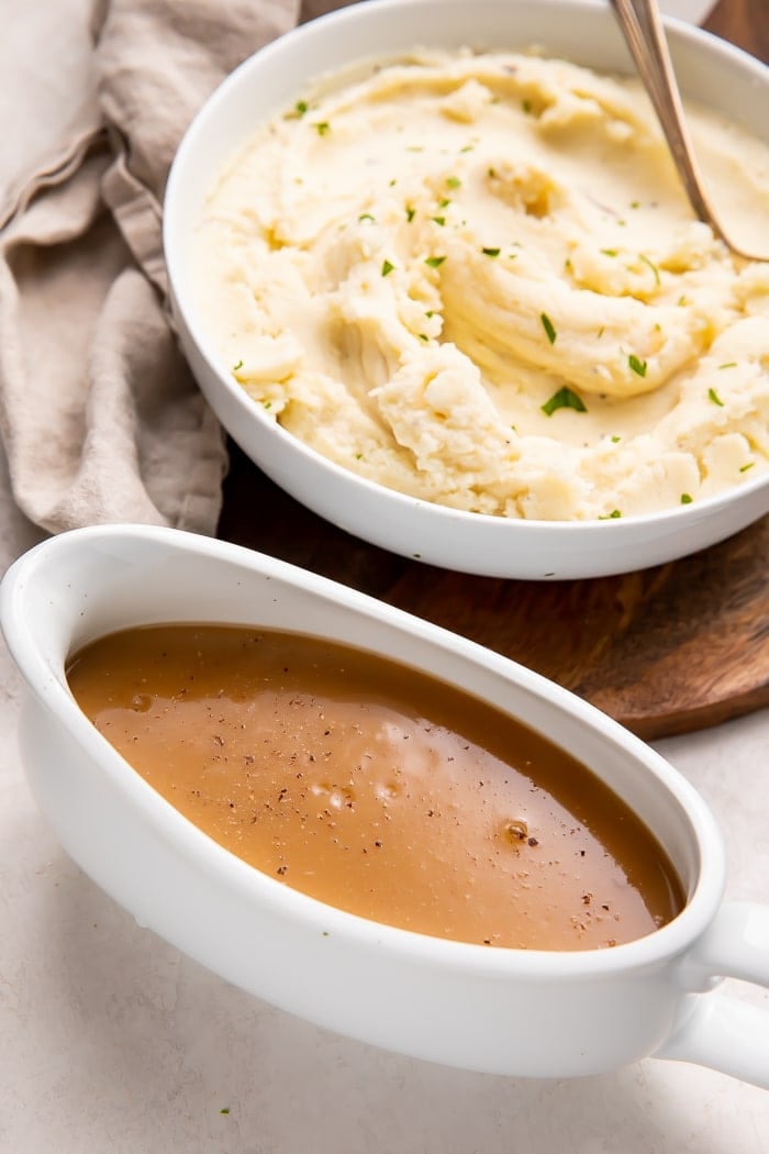Brown gravy in a gravy boat next to a bowl of mashed potatoes