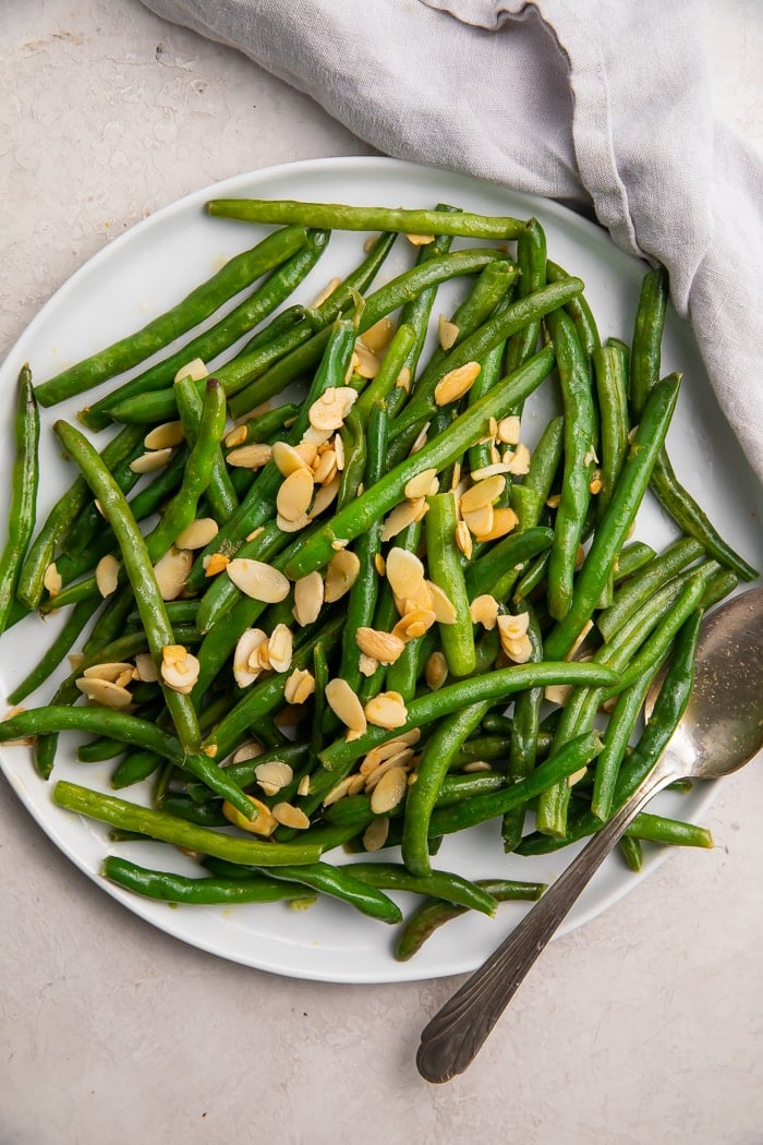 Green beans with almonds on a white platter with a silver fork and white napkin