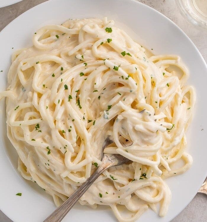 Pasta with keto alfredo sauce on a white plate with a fork