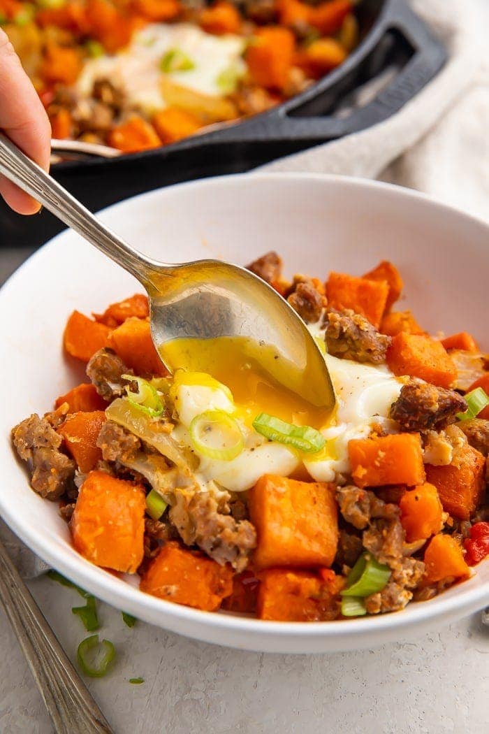 A spoon dipped into a white bowl of sweet potato hash