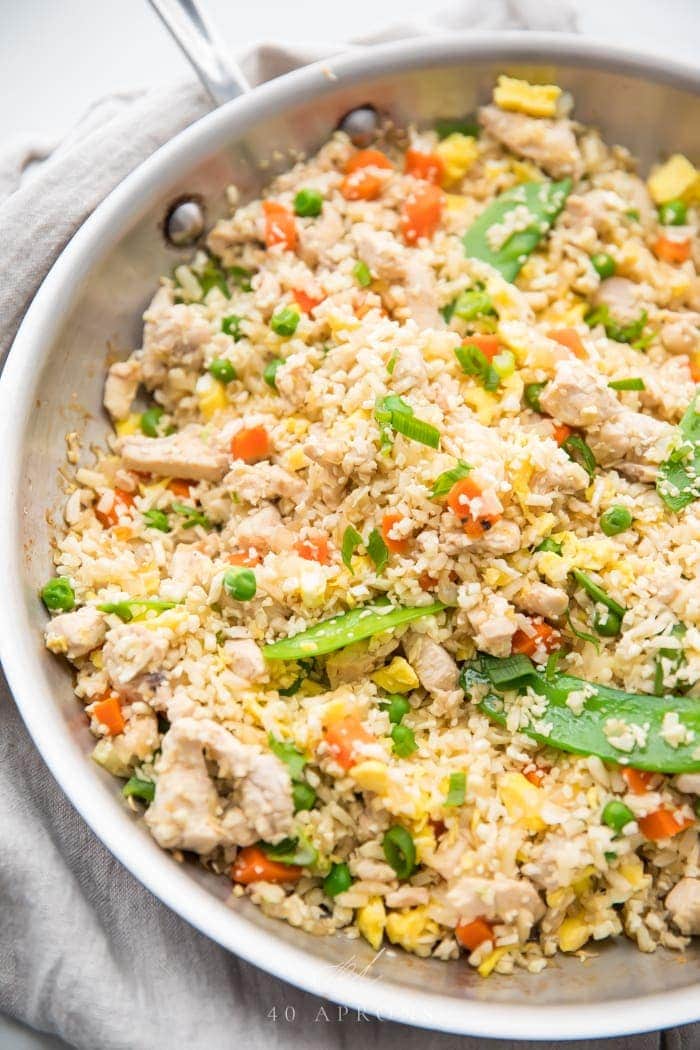 A large white bowl of cauliflower fried rice, veggies, and chicken