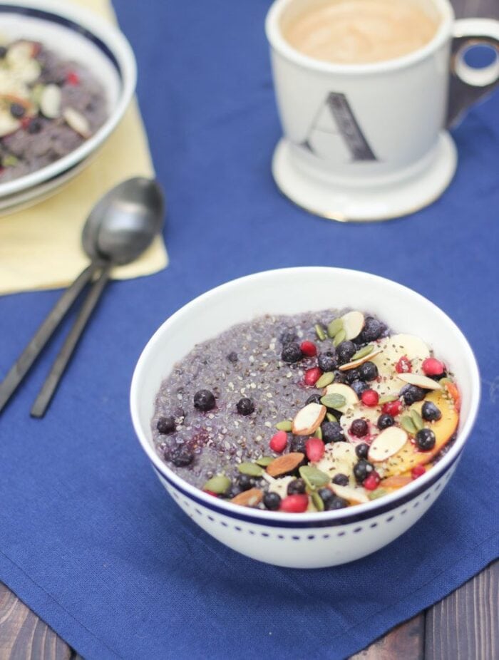 A white bowl of blueberry vegetarian slow cooker quinoa with fruits and slivers of almonds on a blue tablecloth
