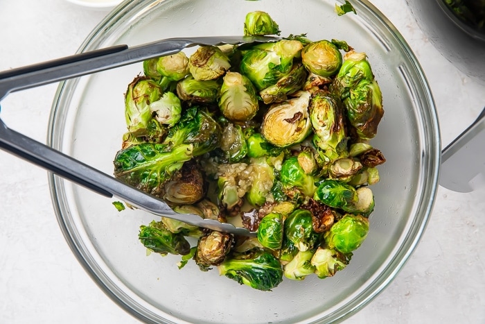 Brussels sprouts in a clear glass bowl with tongs